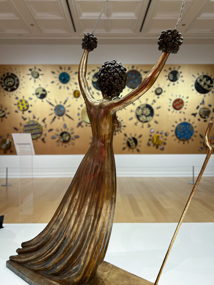 Looking at the back of Salvador Dalí's, Alice in Wonderland, c. 1977-1984 Bronze 46 1/2 x 18 1/16 x 86 1/8 inches (118 x 46 x 219 cm), out of focus in the background is Yinka Shonibare CBE's Bling Painting