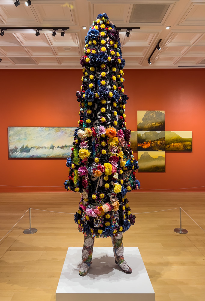 Nick Cave (American, b. 1959) Soundsuit 8:46, 2021 Vintage textile, sequined appliqués, silk flowers, acrylic buttons, metal, and mannequin 98 x 34 x 28 inches (248.92 x 86.36 x 71.12 cm). Cave's Soundsuits mask and create a second skin that conceals race, gender, and class, forcing the viewer to look without judgment, which is often not the case for the life the suits represent. Soundsuit 8:46 represents the lost life of George Floyd. At over eight feet tall, Soundsuit 8:46 features bright floral and patterned textiles, sequins, and acrylic buttons (suitable for a Spring birthing of new life and change - in this case, change is one of social justice). The additional marker of "8:46" in the title refers to how long it took for Floyd to die under Minnesota Officer Chauvin's knee on May 25, 2020.